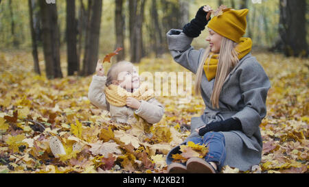 La bionda bambina con la sua mamma passeggiate nel parco di autunno - sono divertenti e raccogliere foglie Foto Stock