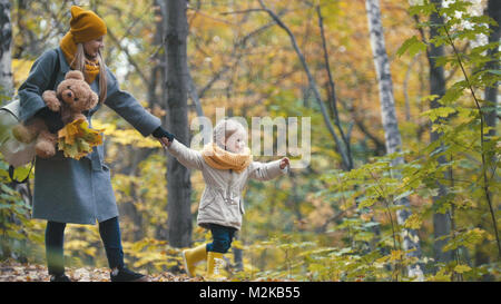 Bella bionda bambina con la sua mamma passeggiate nel parco di autunno - sono divertenti e raccogliere foglie Foto Stock