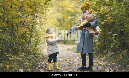 La bionda bambina con la sua mamma passeggiate nel parco di autunno - sono divertenti e raccogliere foglie, close up Foto Stock