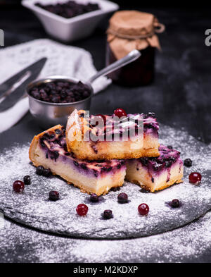 Pezzi di torta di ricotta e mirtilli su uno sfondo nero spolverati con zucchero a velo Foto Stock