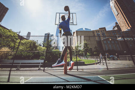 Street basketball atleta di eseguire la grande slam dunk sulla corte, New York sullo sfondo di edifici Foto Stock