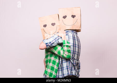 Amore giovane che coprono i loro volti con sacchetto di carta su sfondo bianco. Foto Stock