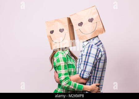 Amore giovane che coprono i loro volti con sacchetto di carta su sfondo bianco. Foto Stock