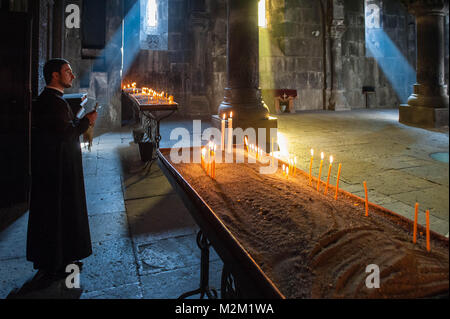 Monaco in attesa a lume di candela nella principale sala della chiesa del Monastero di Geghard. Foto Stock