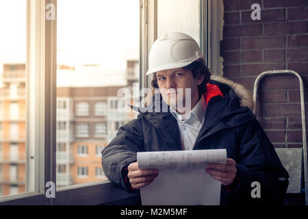 Pensieroso giovane builder in hard hat standng e pensare. Soft focus, tonica Foto Stock