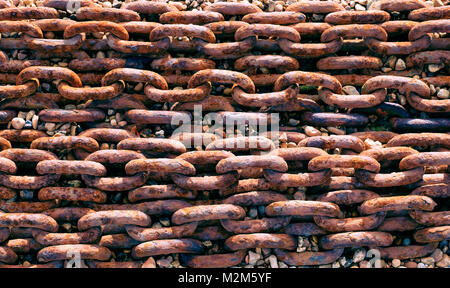 Linee di arrugginita grande catena di metallo su un suolo pietroso beack Foto Stock