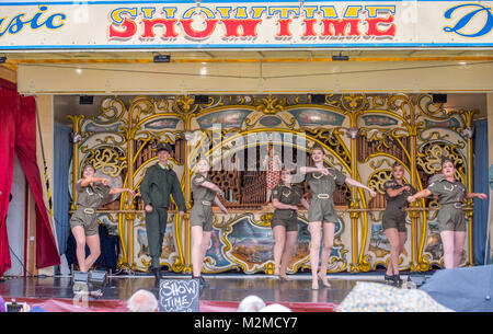 Guarda gli astanti giovani ballerine in abbigliamento militare preforma sulla fiera organo, Masham, North Yorkshire, Regno Unito Foto Stock