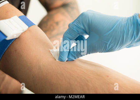 Chiudere l'infermiera puntura per applicazione di lana di cotone con antisettico sul braccio del paziente dopo il prelievo del campione di sangue per il test del sangue Foto Stock