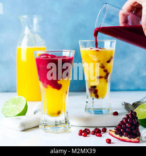 Versando grenadine in due bicchieri di bevande cocktail con liquore all'arancia, spremuta di ananas e succo di melograno e calce e il ghiaccio sul Foto Stock