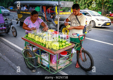 Manila, Filippine - Febbraio 4, 2018 : Una strada fornitore di prodotti alimentari freschi fette di mango verde che vende sul carrello di alimentare a un marciapiede lungo una strada nella città di Manila Foto Stock