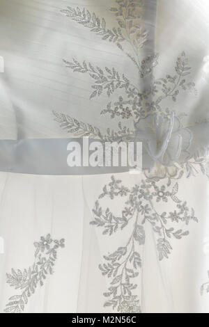 Un delicato merletto tessuto bianco di abito da sposa di sposa con ricami in forma floreale trasparente alla luce del giorno Foto Stock