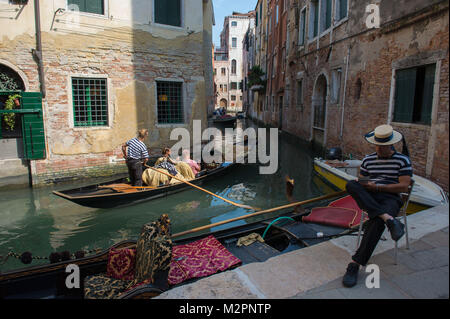 Venezia, Italia. Gondola tenendo i turisti in un canale e gondoliere in attesa per i clienti. Foto Stock