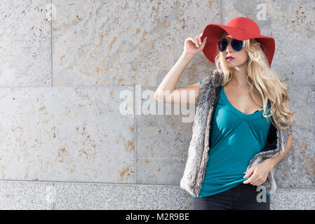 Giovane donna vicino Red Hat e occhiali da sole al di fuori, pongono, semi-ritratto Foto Stock