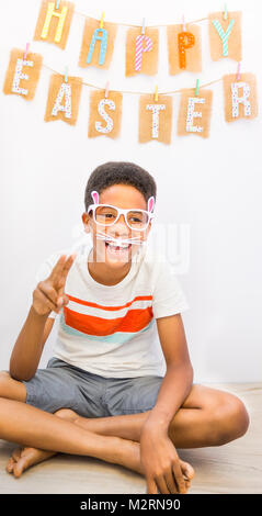 Carino African American black boy coniglietto di indossare occhiali da sole di Coniglio con orecchie di ridere mentre si effettua il simbolo di pace con le sue dita. Felice Pasqua banner Foto Stock