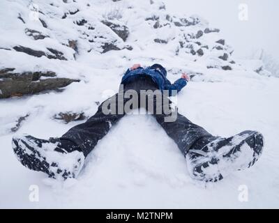 Ragazzo divertente in posa il cumulo di neve. Kid giochi fresco in polvere di neve su terreni sassosi hill. Tempesta di neve e nebbioso meteo. Foto Stock