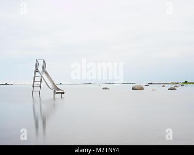 Tramonto a riva e vecchia diapositiva di acciaio nel lago. Chrome scala a torre con la pista di scorrimento, grandi massi di granito intorno a. Autunno freddo mattino con acqua liscia le Foto Stock