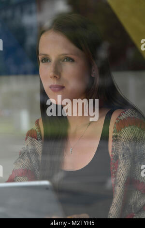 Giovane donna dietro la finestra sul computer portatile presso il café, ritratto Foto Stock