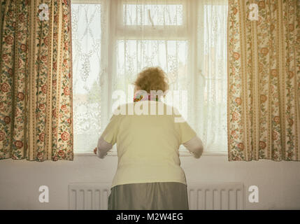 Donna di novanta anni con mano sul radiatore che guarda fuori dalla finestra. REGNO UNITO. Coronavirus, autoisolamento, distanza sociale, quarantena... concetto Foto Stock