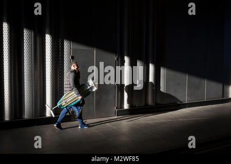 Un uomo porta un asse da stiro mentre passa attraverso un albero di luce del sole, il 7 febbraio 2018, a Londra, in Inghilterra. Foto Stock