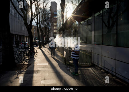 Un vaper espira una nuvola di fumo in condizioni di intensa luce solare in inverno, su un central London street, il 6 febbraio 2018, a Londra, in Inghilterra. Foto Stock