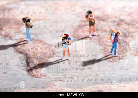 Un gruppo di giovani viaggiatori in miniatura figurine persone con zaini su una mappa del mondo in piedi su un assortimento di destinazioni in un concetto di viaggio e explor Foto Stock