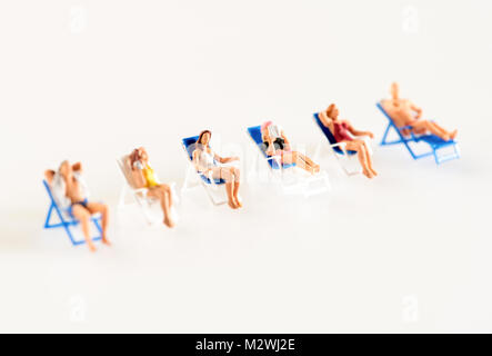 Linea diagonale con copia al di sopra dello spazio bianco del popolo in miniatura, uomini e donne, relax sulla sdraio per prendere il sole in un concetto di una vacanza estiva Foto Stock