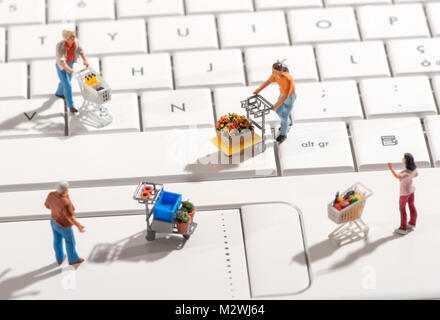 Quattro diverse persone in miniatura con carrelli di shopping su una bianca della tastiera del computer visto elevato angolo con le ombre in un concetto di online o internet sho Foto Stock
