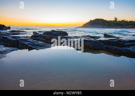 Tramonto su una superficie a specchio su una piccola piscina di roccia nei pressi di piccola spiaggia a Scotts testa sul Nuovo Galles del Sud costa nord dell'Australia Foto Stock