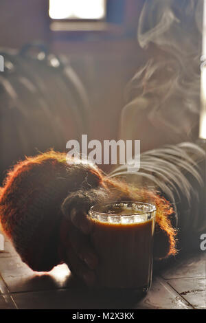 L uomo beve un bicchiere caldo del caffè o del tè per scaldare in baita Foto Stock