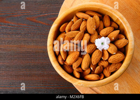 Materie frutta secca di mandorle in una ciotola di legno su una tavola di legno Foto Stock