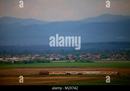 Treno passando attraverso verdi campi bulgara, nuvoloso giorno prima della tempesta Foto Stock