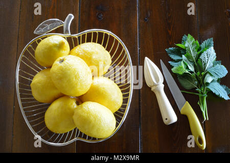 Unwaxd limoni in una forma a mela coppa di frutta, limone spremiagrumi, un coltello e un mazzetto di melissa Foto Stock