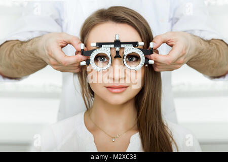 Oculista esaminando donna attraente con all'ottico optometrista telaio di prova. paziente di sesso femminile per verificare la visione in ambulatorio oculistico Foto Stock