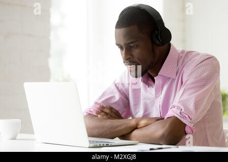 African American uomo che indossa le cuffie utilizzando laptop guardando sullo schermo del computer, sorridente giovane imprenditore nero learning studiare online, guardare vi Foto Stock