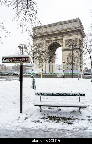 Inverno a Parigi nella neve. L'Arc de Triomphe con un banco di pubblica coperta di neve in primo piano. Foto Stock