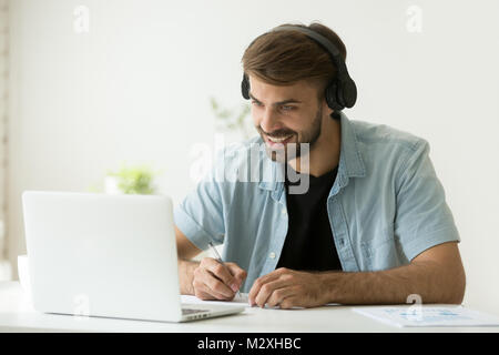 Uomo sorridente che indossano le cuffie guardando lo schermo del computer facendo Foto Stock