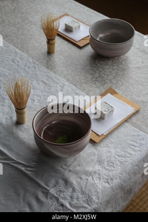 Due cerimonia del tè giapponese set, costituito da un teabowl con verde in polvere macha tea, bambù frusta e torta dolce, su un banco di lavoro, sotto la luce della finestra. Foto Stock