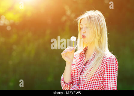 Bella giovane donna soffia semi da un fiore di dente di leone Foto Stock