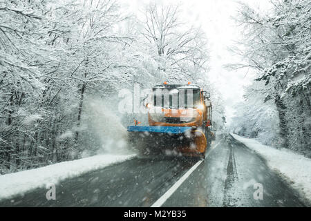 Vista anteriore del servizio spazzaneve carrello gritter e spandimento di sale sulla superficie della strada per impedire la formazione di ghiaccio nella neve tempestoso giorno d'inverno. Foto Stock