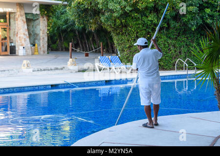 Un uomo, personale a pulire la piscina in un resort tropicale. Foto Stock
