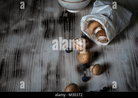 Foto orizzontale con diversi marrone funghi commestibili. Materie gli champignon sono versate dal libro bianco borsa su vintage tavola di legno. Pochi blackthorns con d Foto Stock