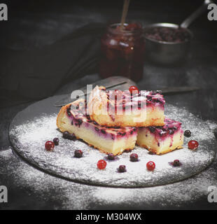 Pezzi di torta di ricotta e mirtilli su uno sfondo nero spolverati con zucchero a velo Foto Stock
