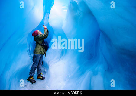Donna Fotografa in una caverna di ghiaccio nel ghiacciaio Fox, Isola del Sud, Nuova Zelanda