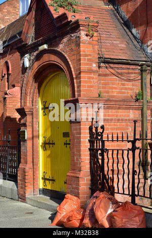 Città di arancia consiglio di plastica sacchi della spazzatura davanti a casa in mattoni rossi con giallo brillante porta vintage. Foto Stock