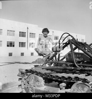 Una giovane donna in un costume da bagno si siede su un bulldozer, ca. 1948. Foto Stock