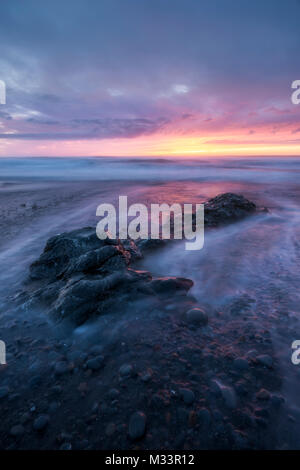 Un tramonto mozzafiato si illumina Westport Beach come flussi di acqua intorno a un masso sul Mendocino litorale della California del Nord. Foto Stock