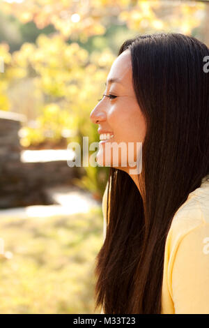 Felice bella donna asiatica sorridente seduto fuori. Foto Stock