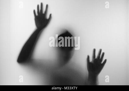 Orrore donna dietro il vetro opaco in bianco e nero. Sfocata le mani e il corpo nella figura di destra.Halloween sfondo.foto in bianco e nero Foto Stock