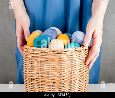 La donna nel vestito blu tenendo premuto il cestello con colorate in giallo le uova di pasqua Foto Stock