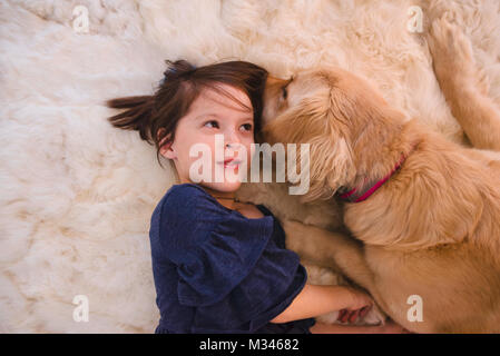 Ragazza distesa sul pavimento a giocare con il suo golden retriever cane Foto Stock